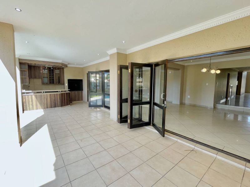 Spacious open-plan living area featuring tiled flooring, recessed lighting, and bi-fold doors leading to the exterior, complete with a built-in bar area.