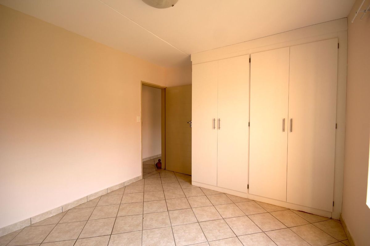 A clean, empty bedroom featuring neutral wall paint, tiled flooring, and ample built-in cupboard storage space.