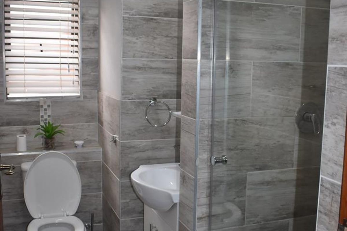 Modern bathroom featuring floor-to-ceiling wood-look tiling, a glass-enclosed walk-in shower, a wall-mounted toilet, and a compact vanity basin.