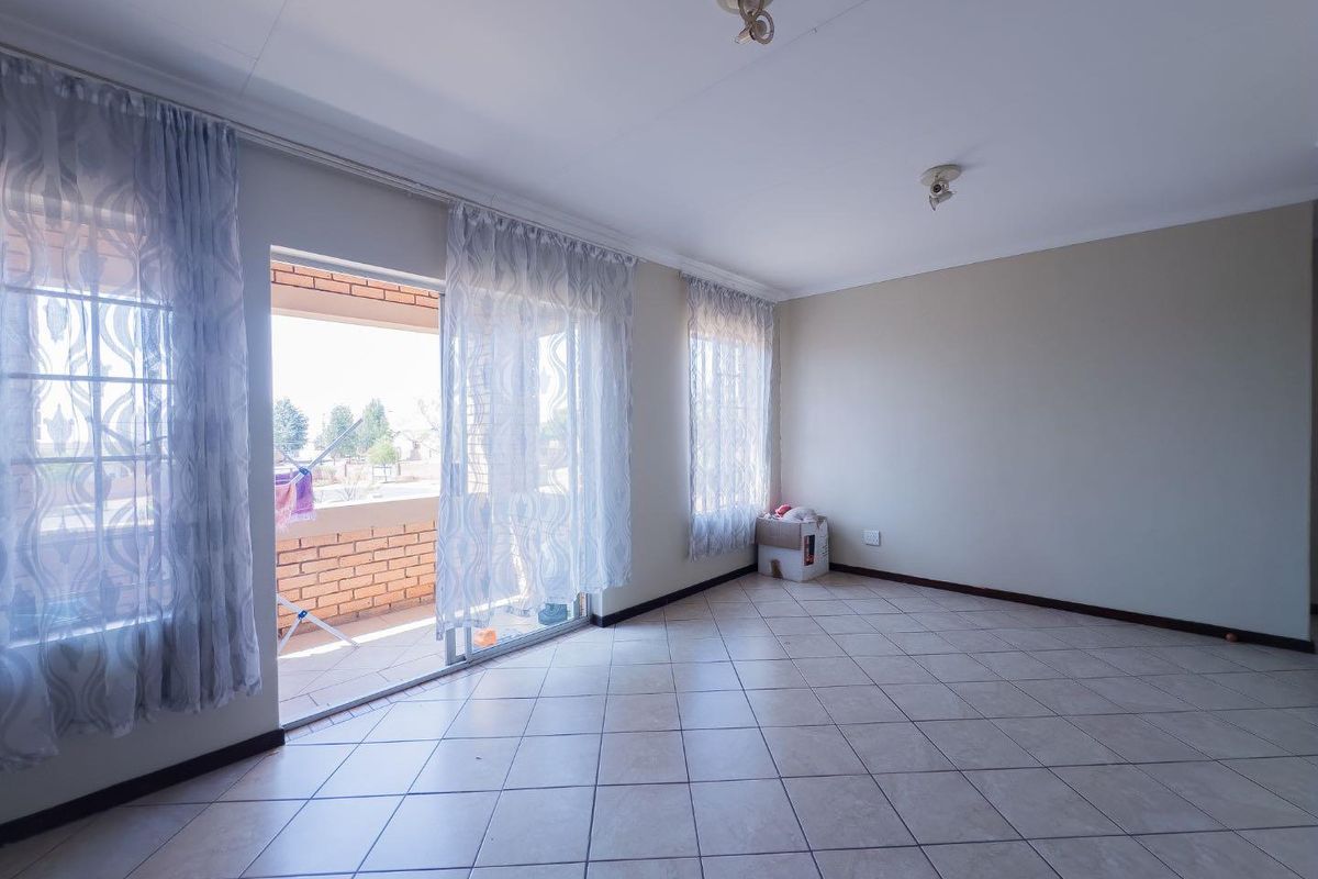 Spacious living area featuring neutral ceramic floor tiles, large windows, and sliding glass doors providing direct access to an outdoor patio.