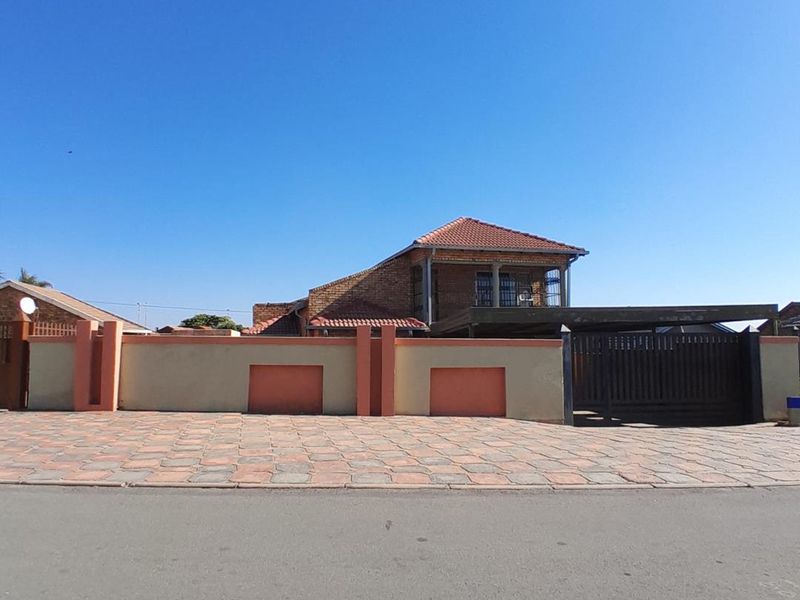 Front view of a double-story house featuring a paved driveway, perimeter wall with gate, and a covered carport area.