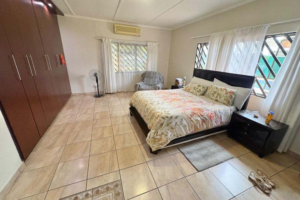 Spacious bedroom featuring large built-in wooden wardrobes, tiled flooring, and wall-mounted air conditioning unit with natural light from multiple windows.