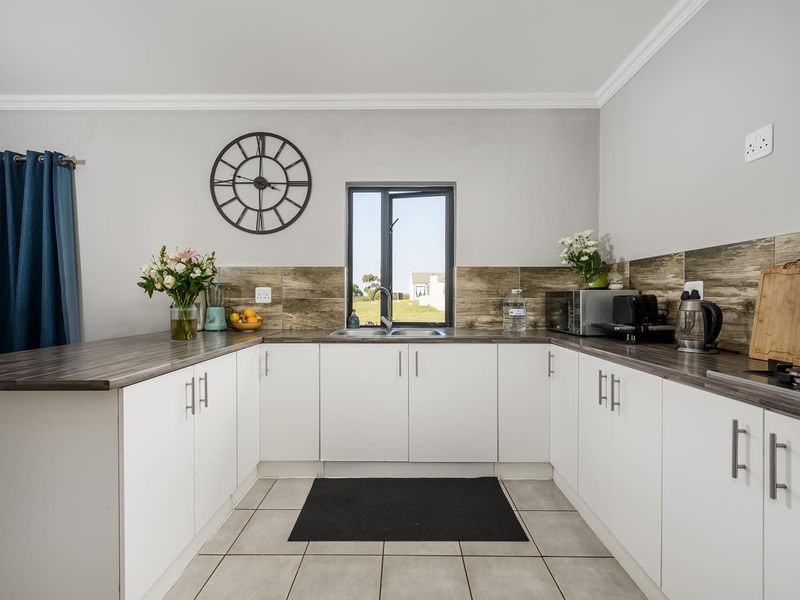 A well-maintained kitchen featuring white cabinetry, wood-look laminate countertops, a tiled backsplash, and a functional U-shaped layout with a central sink.