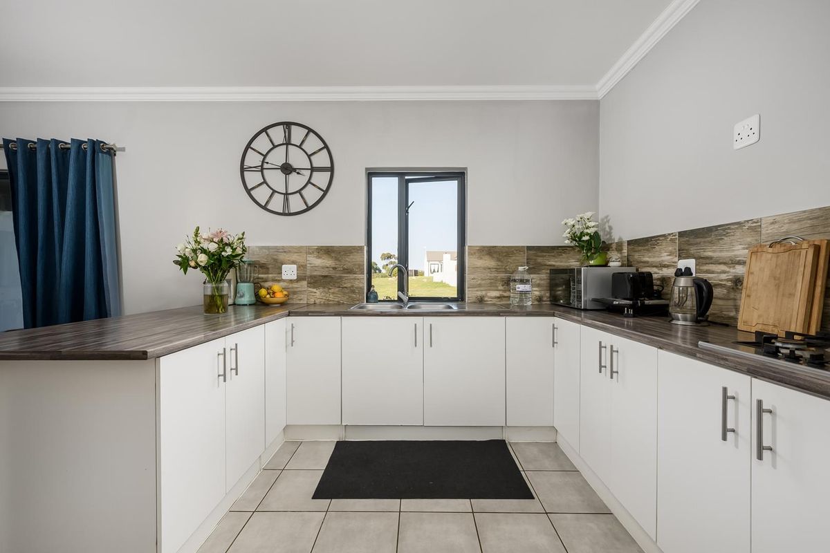 A well-maintained kitchen featuring white cabinetry, wood-look laminate countertops, a tiled backsplash, and a functional U-shaped layout with a central sink.