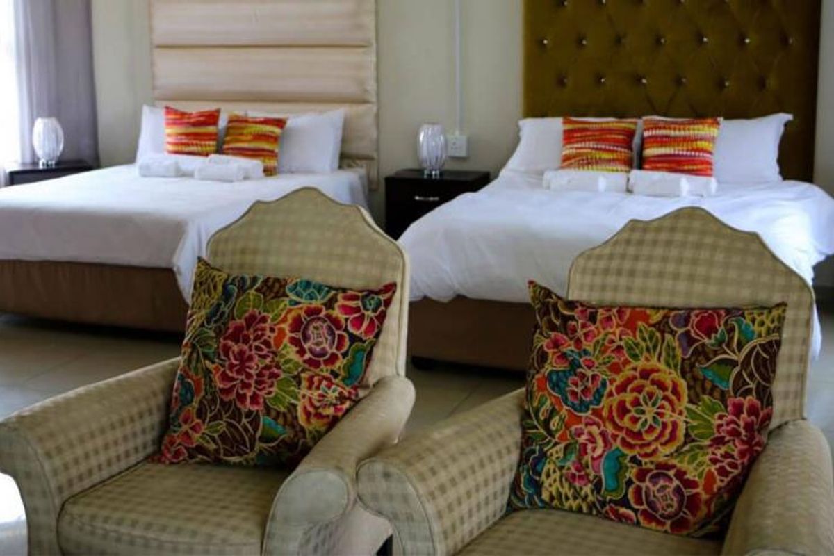 A spacious bedroom featuring two double beds with upholstered headboards and tiled flooring, suitable for guest accommodation.