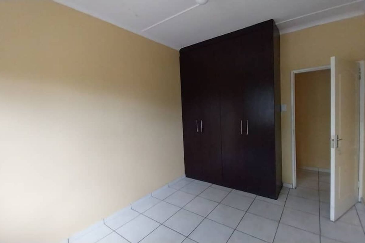 A simple bedroom featuring tiled flooring and a built-in dark wood wardrobe, offering a functional and neutral space.