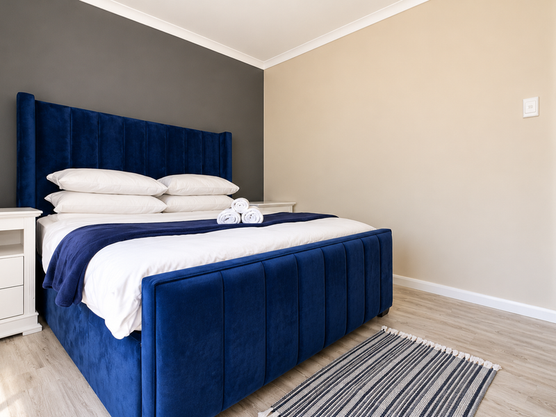 A well-maintained bedroom featuring light laminate flooring, a neutral color palette with a dark accent wall, and clean architectural finishes.