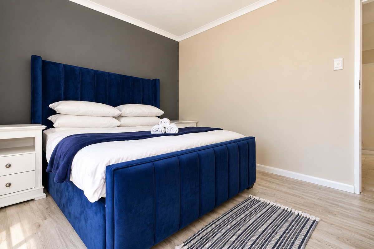 A well-maintained bedroom featuring light laminate flooring, a neutral color palette with a dark accent wall, and clean architectural finishes.