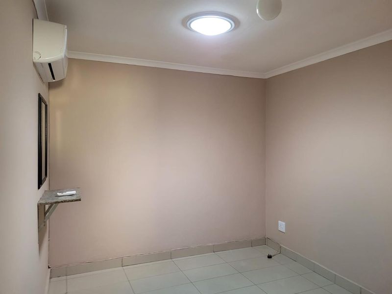 A clean, empty bedroom featuring tiled flooring, a wall-mounted air conditioning unit, and a small built-in shelf.