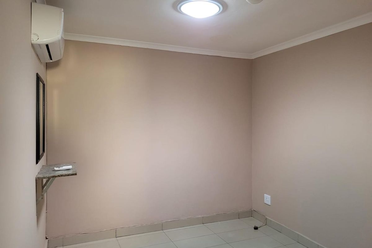 A clean, empty bedroom featuring tiled flooring, a wall-mounted air conditioning unit, and a small built-in shelf.