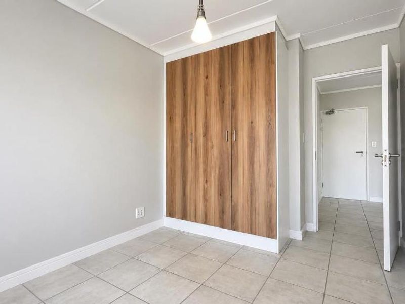 A clean, empty bedroom featuring modern wood-finish built-in cupboards, neutral grey walls, and light-colored floor tiles.