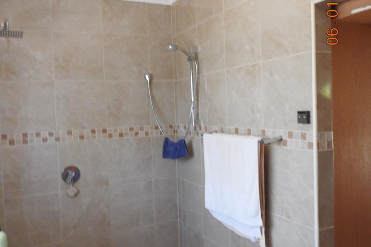 A walk-in shower area featuring neutral wall tiles, a mosaic tiled floor, and a wall-mounted shower head with a handheld attachment.