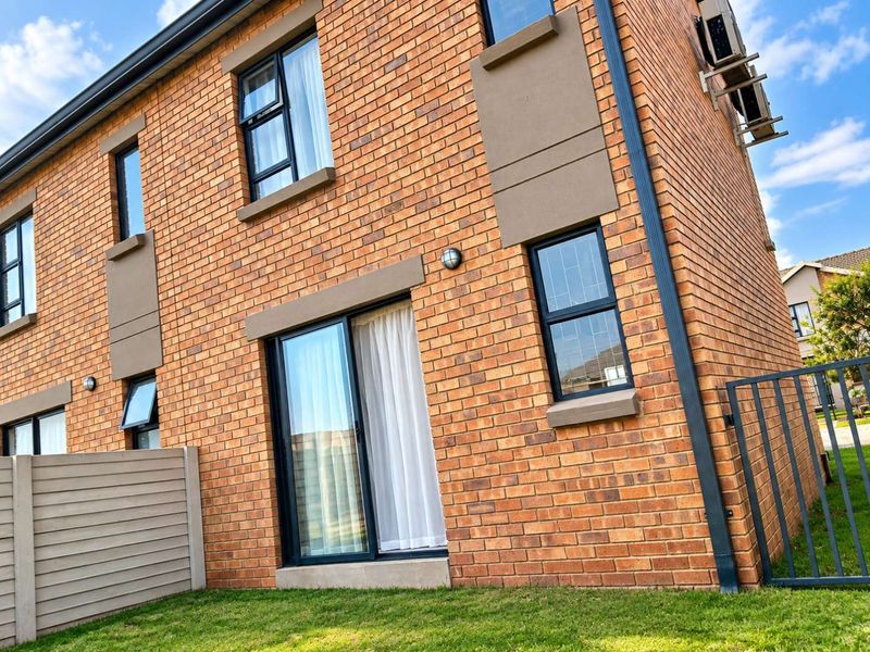 Rear view of a modern face brick townhouse featuring aluminium window frames, a sliding glass door, and a private garden area.