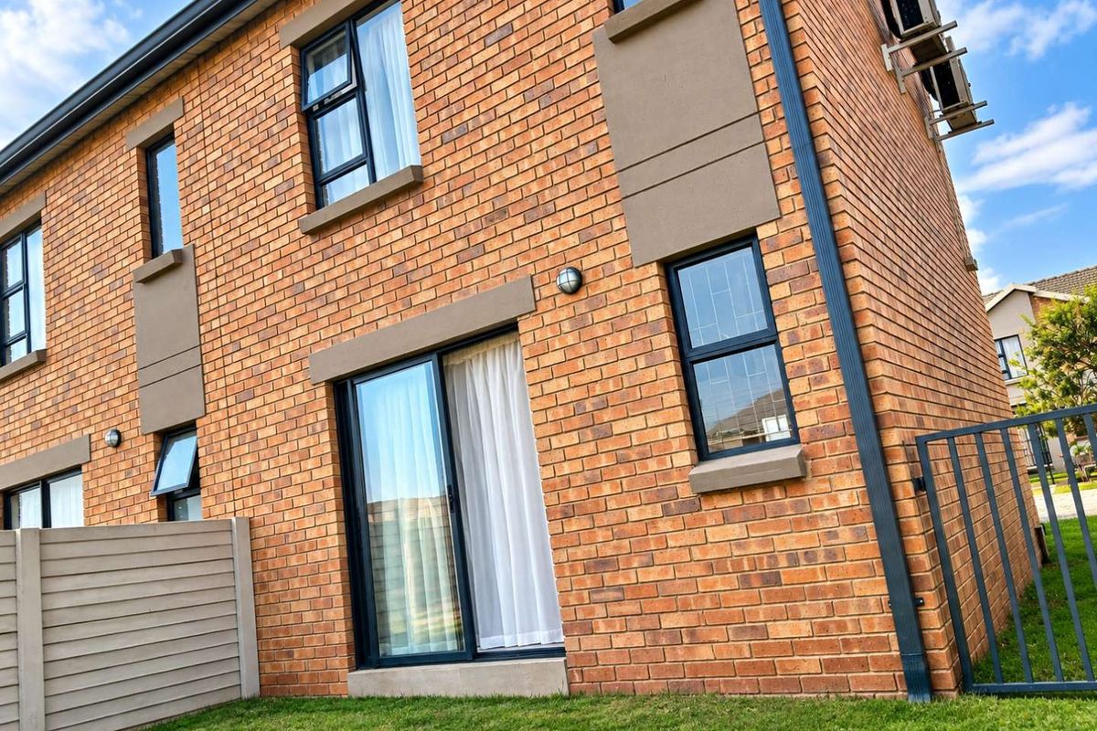 Rear view of a modern face brick townhouse featuring aluminium window frames, a sliding glass door, and a private garden area.