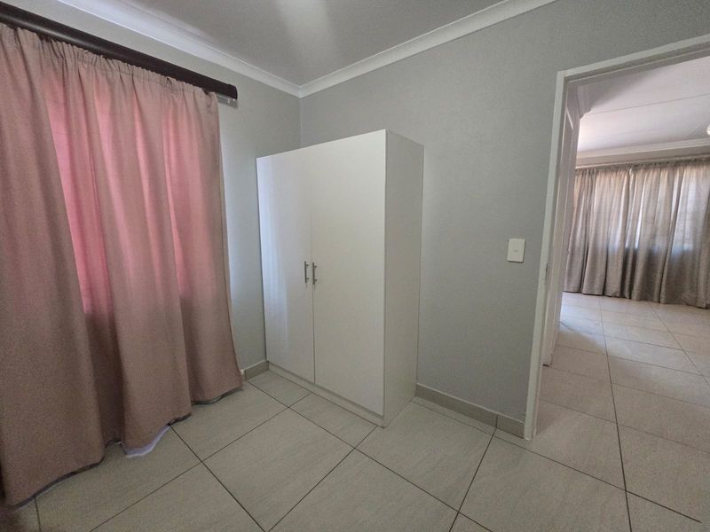 A bedroom featuring neutral tiled flooring, a built-in cupboard, and access to an adjacent room.