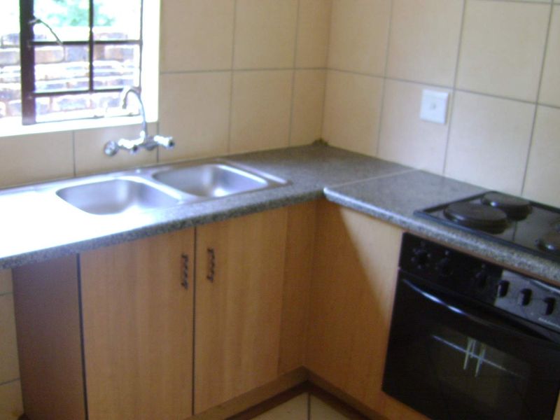 A functional kitchen featuring laminate countertops, a double bowl stainless steel sink, built-in oven, electric hob, and timber veneer cabinetry with tiled splashbacks.