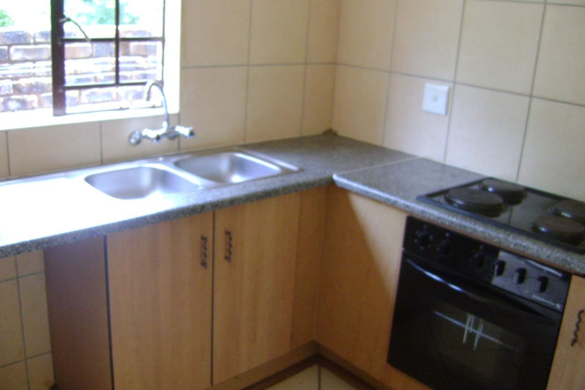 A functional kitchen featuring laminate countertops, a double bowl stainless steel sink, built-in oven, electric hob, and timber veneer cabinetry with tiled splashbacks.
