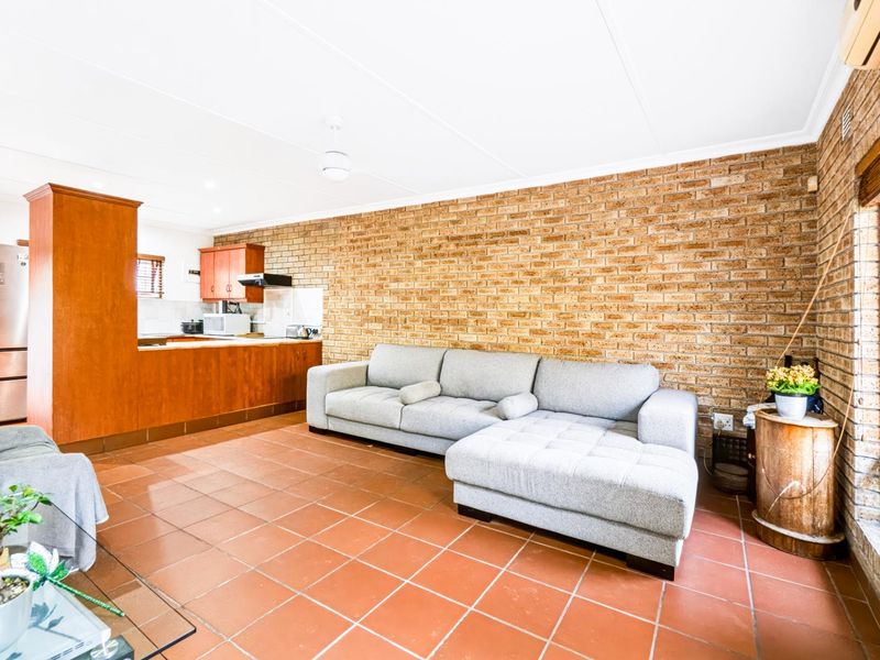 Open-plan living area featuring exposed brick walls, ceramic tile flooring, and an integrated kitchen with wooden cabinetry and an extractor fan.