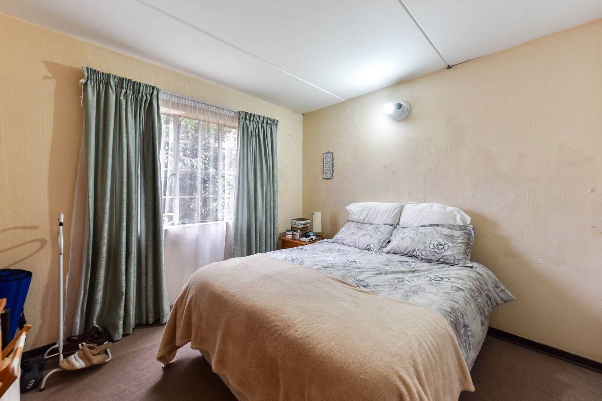 A bedroom featuring a window with curtains and a wall-mounted light fixture, requiring cosmetic updates to the wall finishes.