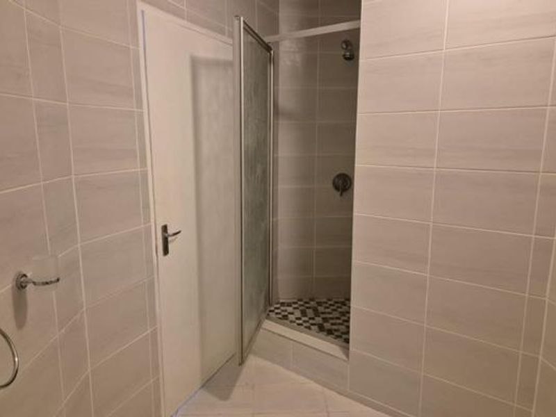 A clean, modern bathroom featuring neutral wall tiles, a tiled floor, and a glass-enclosed shower stall with fixed shower fixtures.
