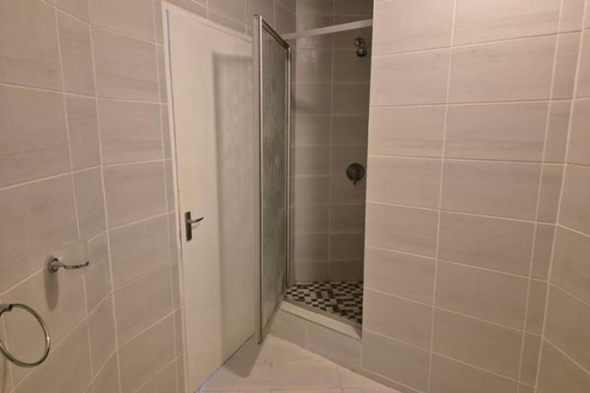 A clean, modern bathroom featuring neutral wall tiles, a tiled floor, and a glass-enclosed shower stall with fixed shower fixtures.