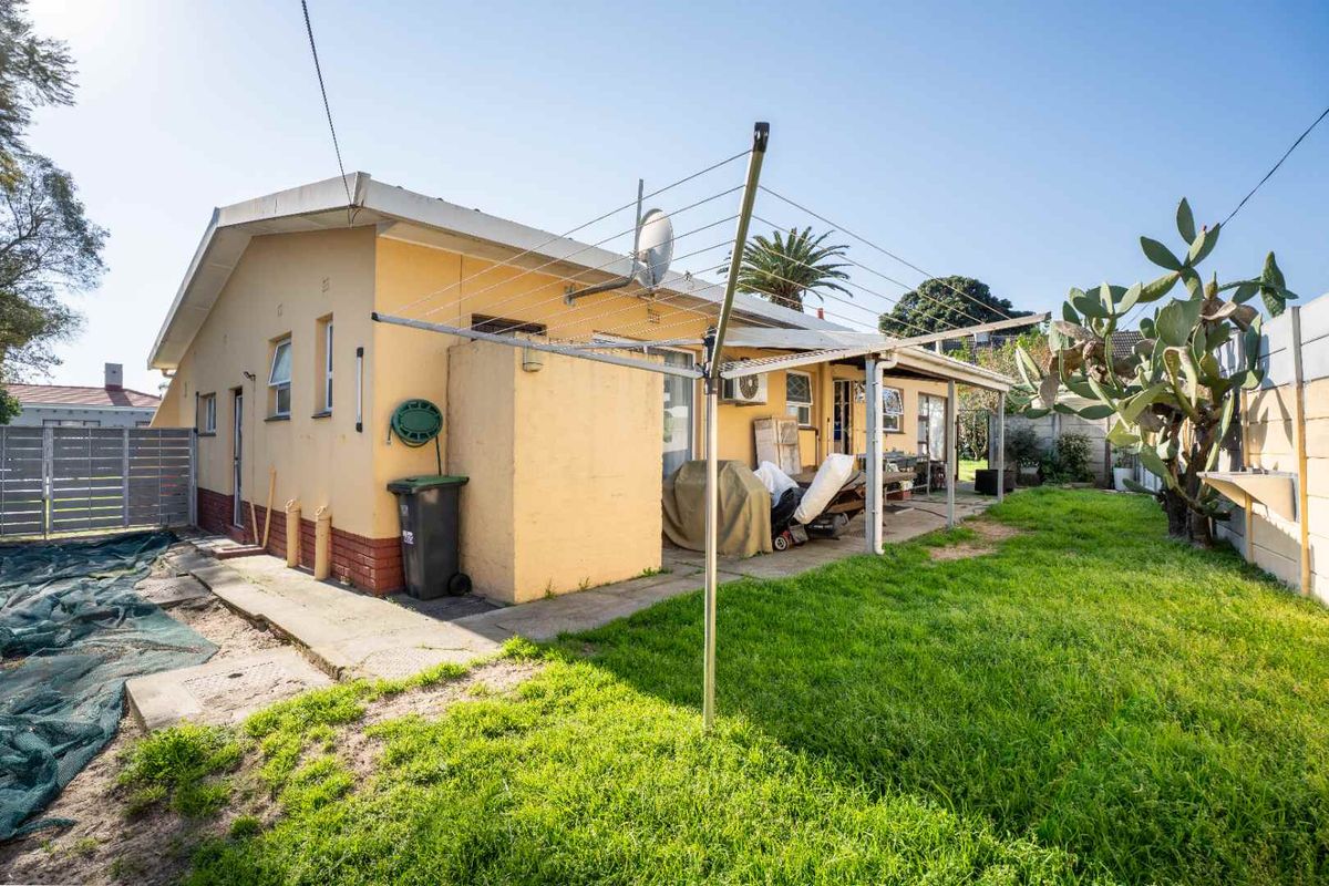 Rear exterior view of the property featuring a covered patio area, lawn, boundary wall, and basic utility fixtures.