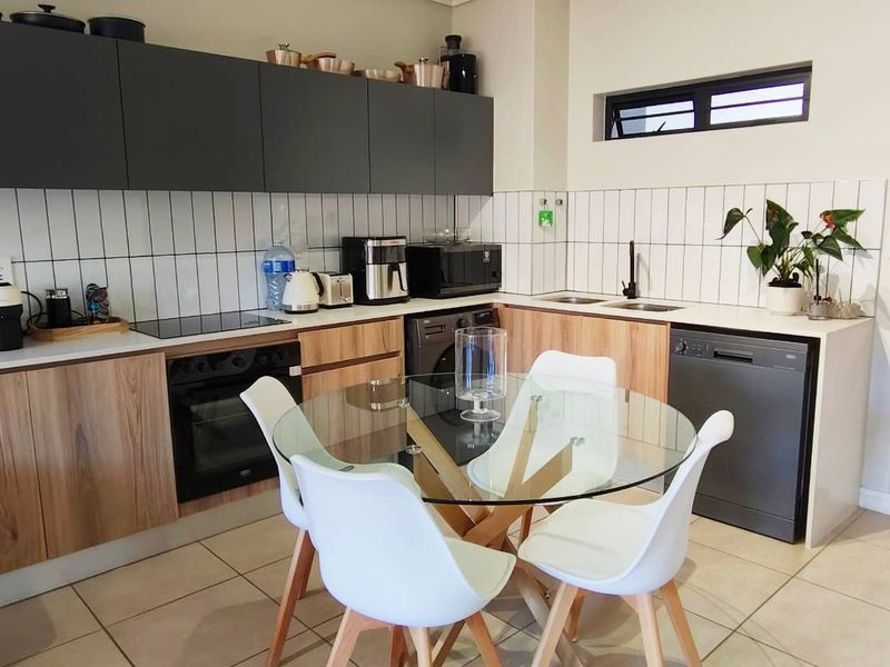 Modern open-plan kitchen featuring wood-grain lower cabinets, dark matte upper cabinetry, subway tile backsplash, and integrated appliances with tiled flooring.