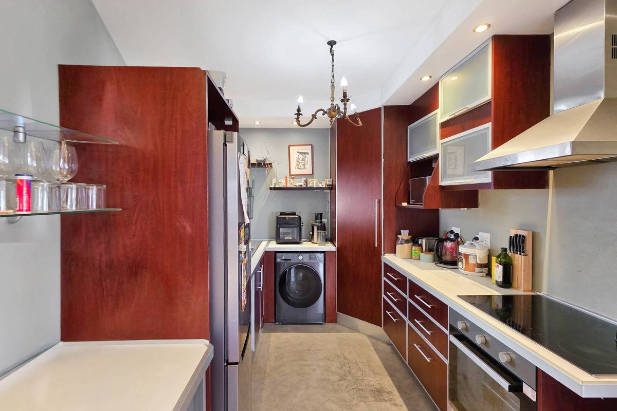 A functional galley-style kitchen featuring dark wood cabinetry, integrated appliances, a built-in oven with hob, and dedicated space for laundry equipment.
