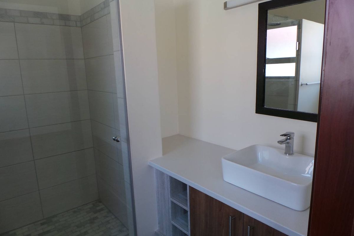 Modern bathroom featuring a glass-enclosed shower with tiled walls and a vanity unit with a vessel sink and wall-mounted mirror.