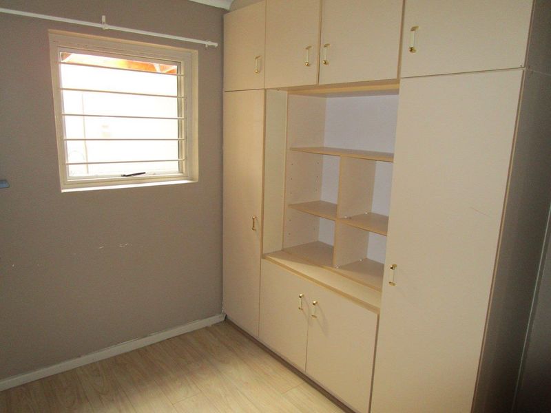 A bedroom featuring laminate flooring, a window with security bars, and extensive built-in cupboard storage.