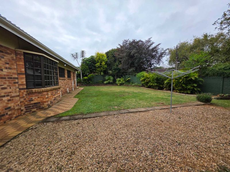 A spacious rear garden featuring a well-maintained lawn, paved walkway, gravel area, and perimeter boundary wall, providing a private outdoor space.