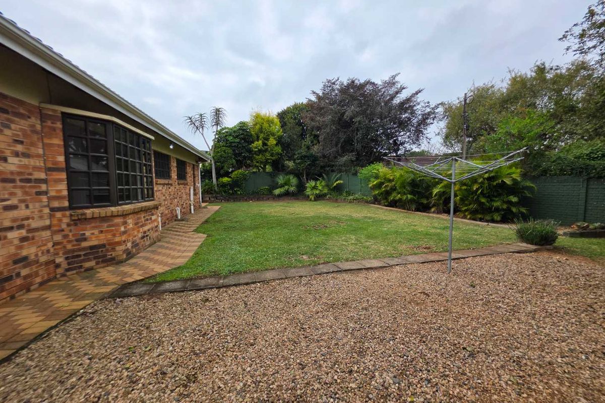 A spacious rear garden featuring a well-maintained lawn, paved walkway, gravel area, and perimeter boundary wall, providing a private outdoor space.