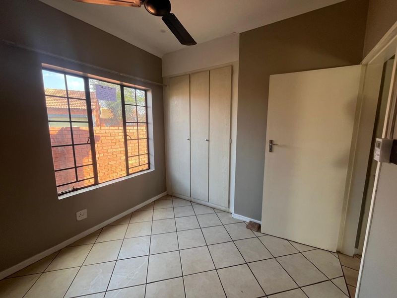 A vacant bedroom featuring tiled flooring, built-in cupboards, and a ceiling fan, offering a neutral canvas for personalization.
