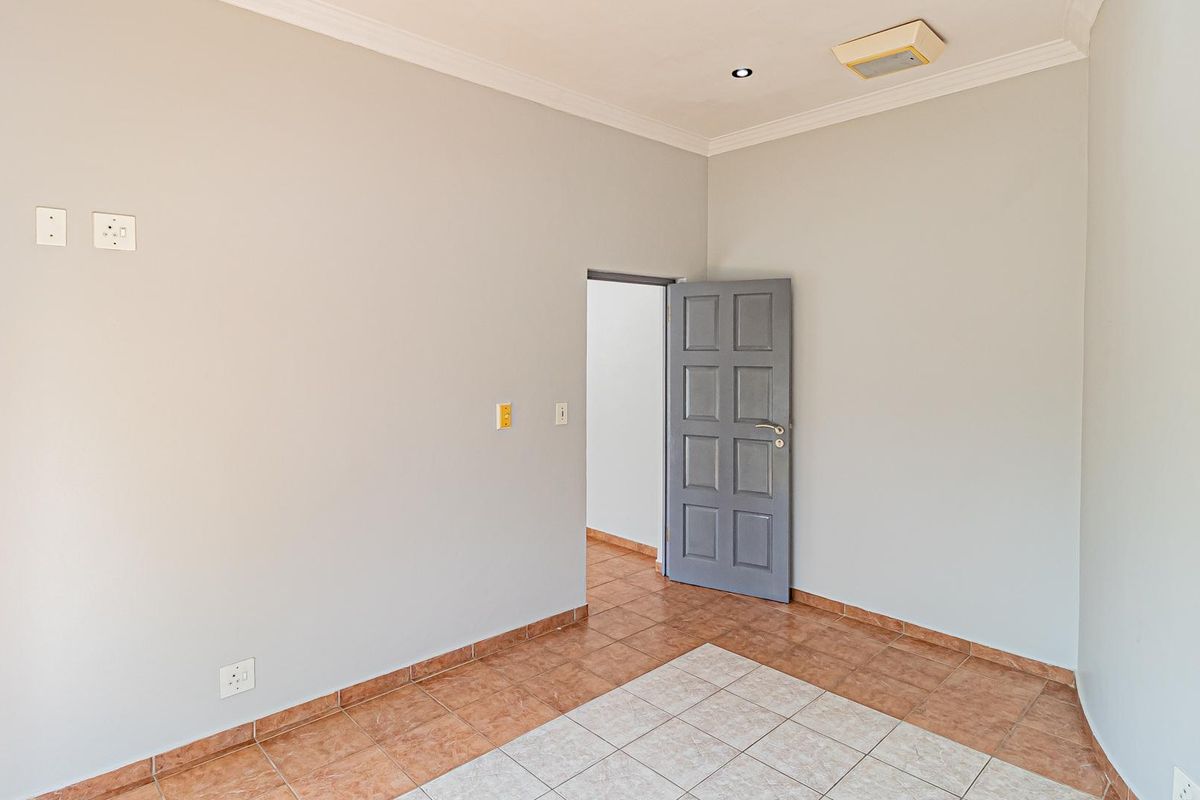 A vacant bedroom featuring neutral walls, tiled flooring, and a classic panelled door, offering a clean and versatile space ready for personalization.