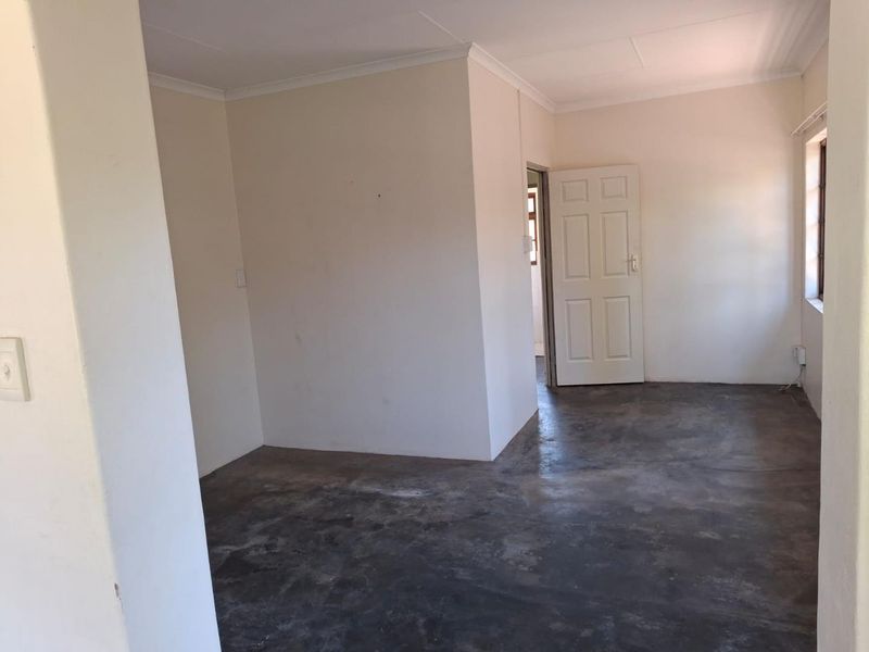 An empty living area featuring plain walls, cove cornicing, and exposed concrete flooring, offering a blank canvas for renovation.