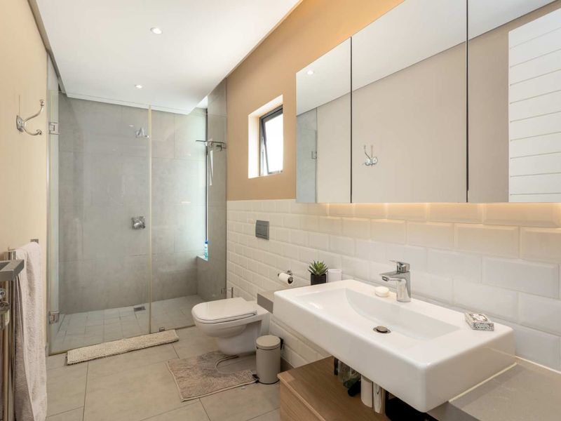 Modern bathroom featuring a walk-in shower with glass screen, wall-mounted toilet, vanity basin, and a large mirrored medicine cabinet with integrated lighting.