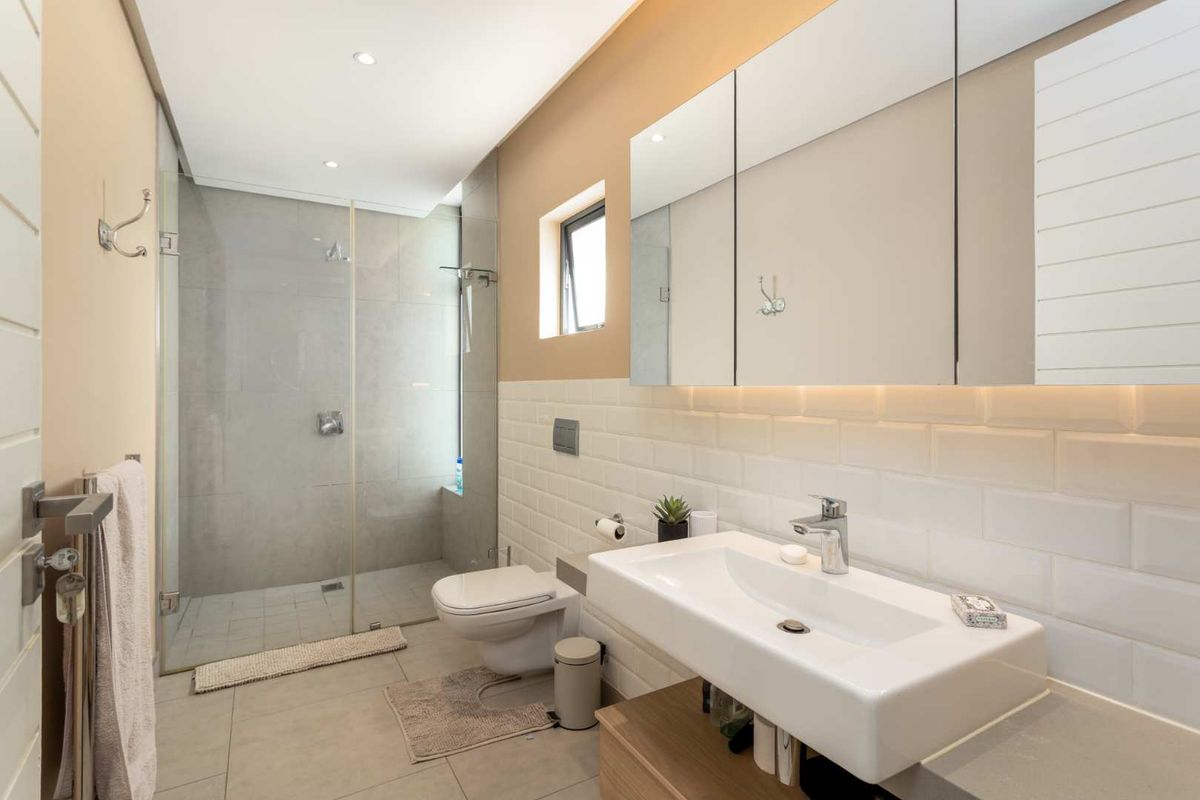 Modern bathroom featuring a walk-in shower with glass screen, wall-mounted toilet, vanity basin, and a large mirrored medicine cabinet with integrated lighting.