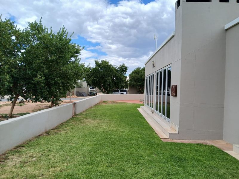 A well-maintained rear garden featuring a manicured lawn, boundary wall, and modern bi-fold doors leading into the home.
