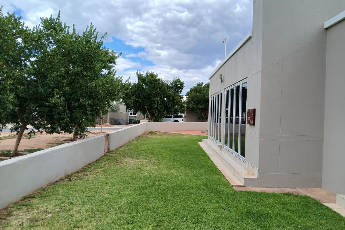 A well-maintained rear garden featuring a manicured lawn, boundary wall, and modern bi-fold doors leading into the home.