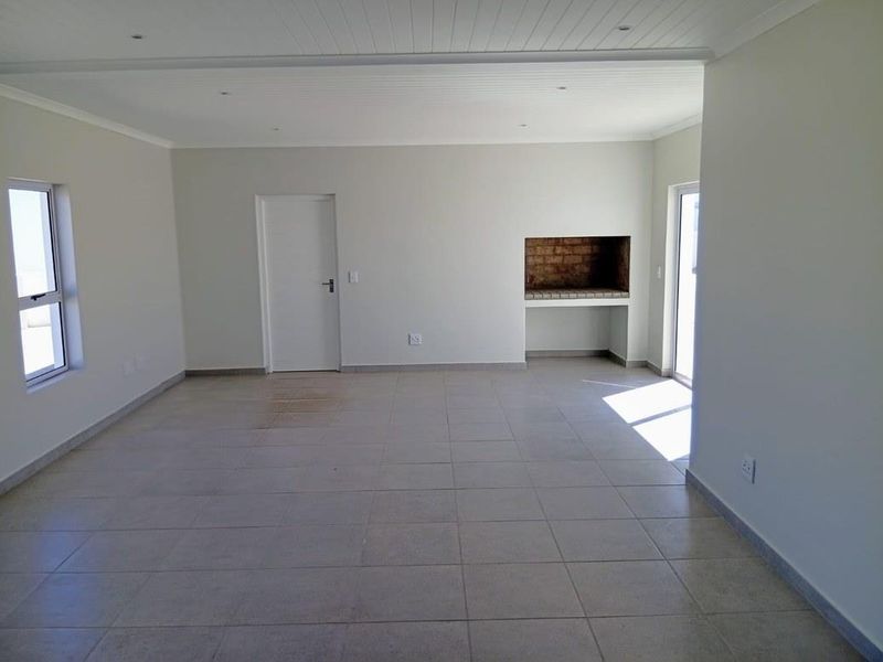Spacious open-plan living area featuring neutral tiled flooring, recessed lighting, and a built-in indoor braai, offering a versatile blank canvas for your interior design.