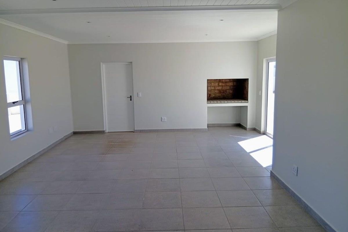 Spacious open-plan living area featuring neutral tiled flooring, recessed lighting, and a built-in indoor braai, offering a versatile blank canvas for your interior design.