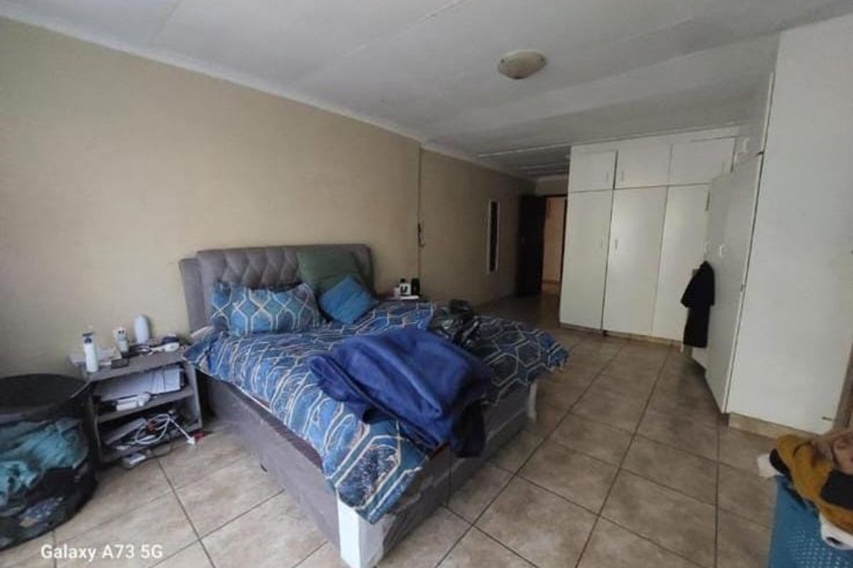 Spacious bedroom featuring built-in cupboards and tiled flooring, offering a functional layout with potential for cosmetic updates.