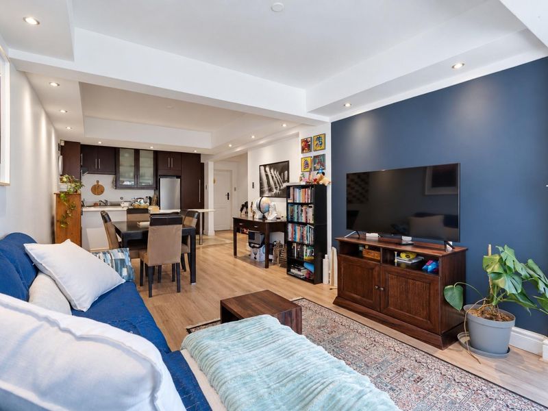 Open-plan living and dining area featuring laminate flooring, recessed lighting, a dark blue accent wall, and an integrated kitchen with dark cabinetry.