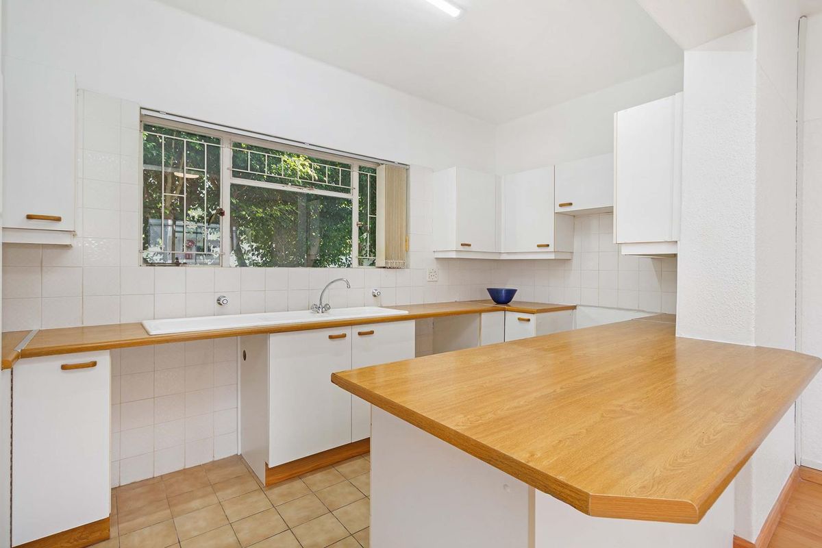 A functional, empty kitchen featuring white cabinetry, laminate countertops, a double basin sink, and tiled backsplash with natural light from a window.