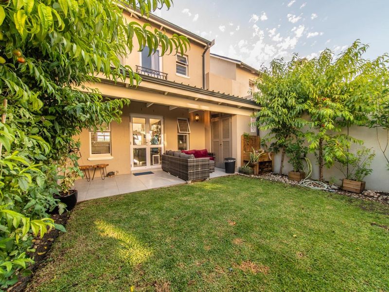 A well-maintained rear garden featuring a covered patio area with tiled flooring, established trees, and a neat lawn, providing a pleasant outdoor living space.