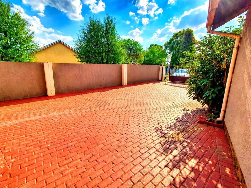 A paved front driveway area enclosed by a boundary wall and metal gate, providing secure off-street parking space.