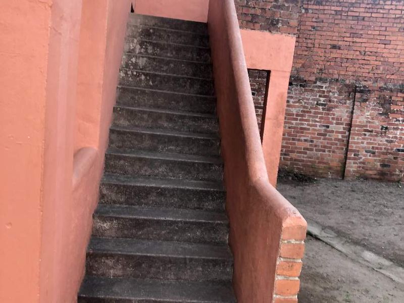 Exterior view of a concrete staircase leading to an upper level, featuring a brick boundary wall with security razor wire.