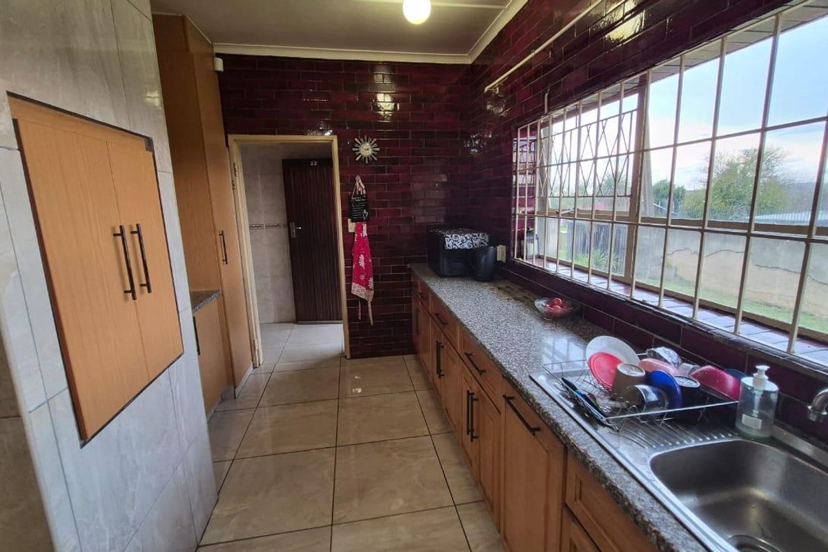 A functional kitchen featuring granite countertops, built-in wooden cabinetry, and a large window with security bars overlooking the exterior.