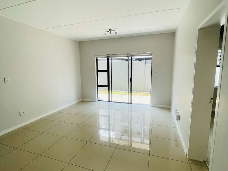 A bright and spacious open-plan living area featuring neutral tiled flooring, modern ceiling spotlights, and large sliding glass doors leading to the exterior.