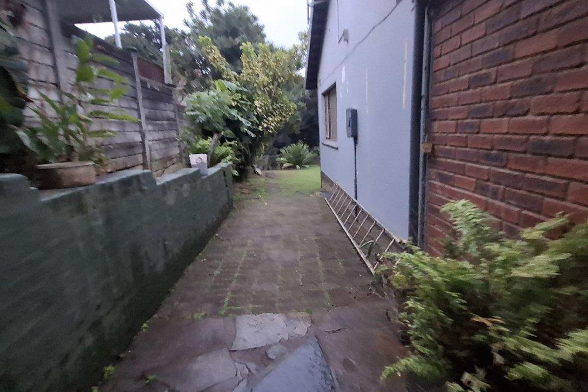 A narrow side passage featuring a paved walkway, brick walling, and a retaining wall along the side of the house.